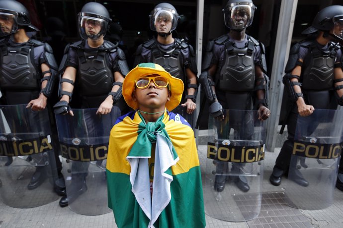 A boy wrapped in Brazilian national flag stands in front of policemen and listen
