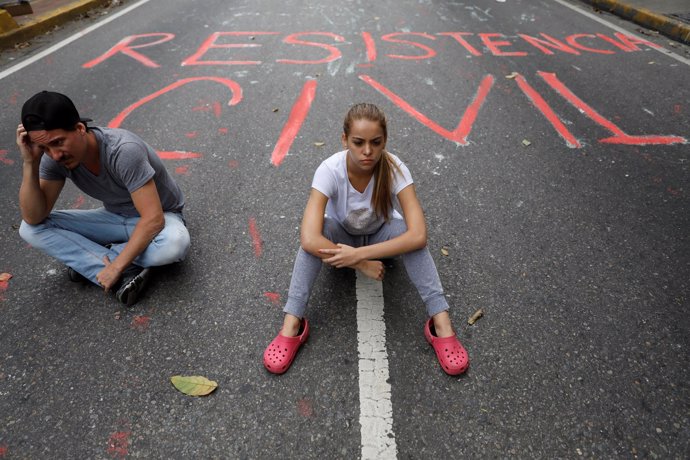 Manifestantes opositores en Caracas con graffiti 'Resistencia Civil'