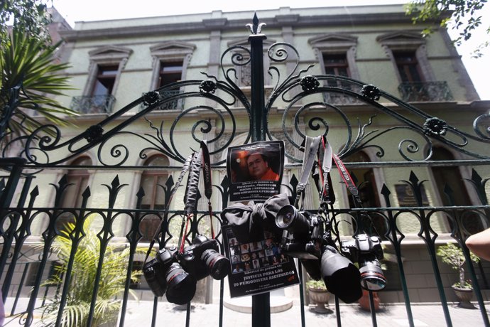 Journalists hang their cameras next to protest posters outside the gates of the 