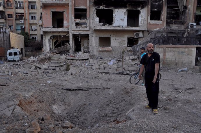 Un hombre señala un crater producido por una bomba barril en Yarmuk (Siria)