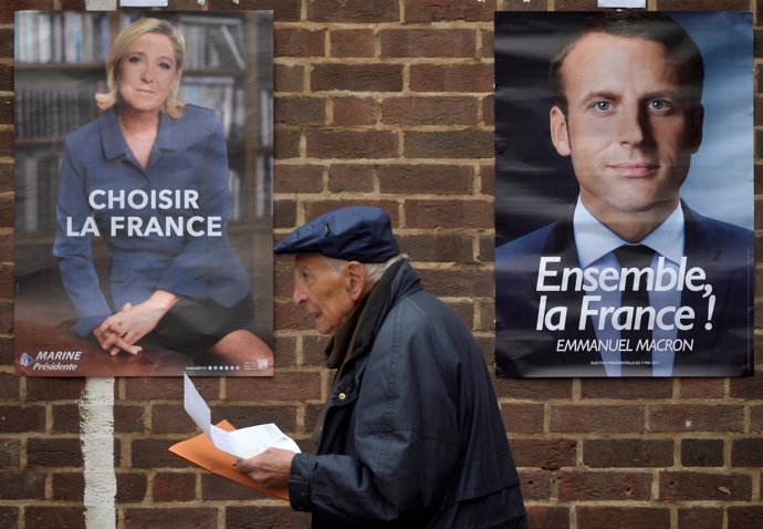 Un hombre pasa entre los carteles electorales de Macron y Le Pen