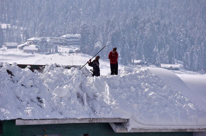 Dos trabajadores retiran nieve en una vivienda en la Cachemira india