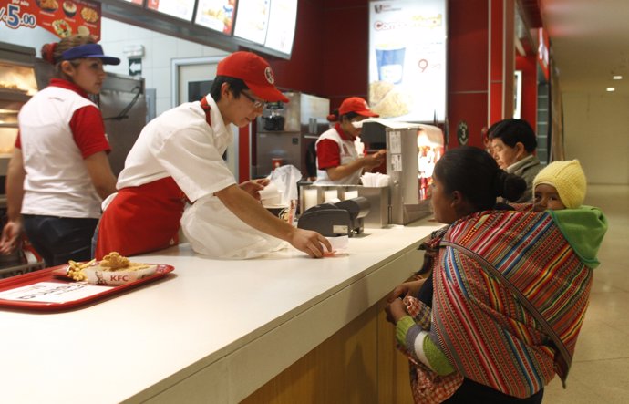 An Andean woman stands at the counter of a foreign fast food restaurant at a sho