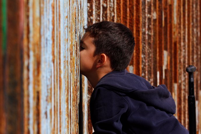 A boy talks to his relatives across a fence separating Mexico and the United Sta