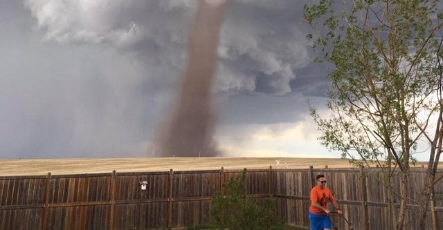 Un hombre pasa de un tornado y corta el césped de su jardín