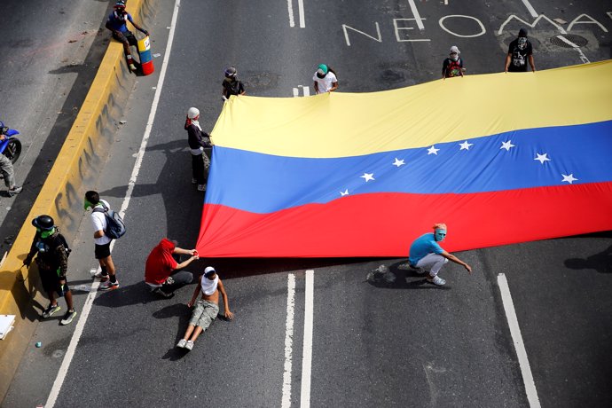 Demonstrators hold a Venezuelan flag as they block a main street during protests