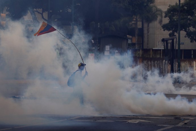 A demonstrator carrying a national flag walks away from tear gas during clashes 