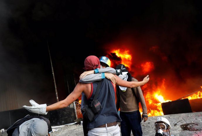 Protesters hug in front of a fire burning at the entrance of a building, housing