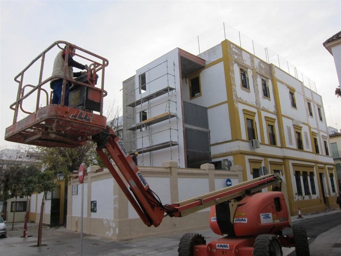 Un operario maneja una grúa junto a un colegio en obras