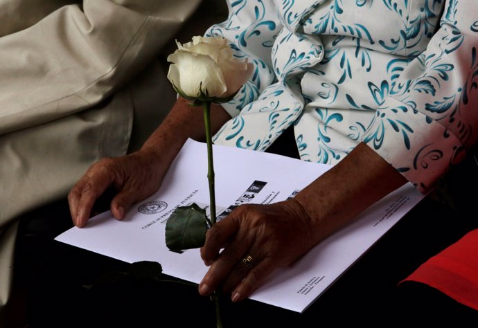 A white rose is held by a relative during a ceremony where the remains of person