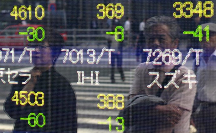 People are reflected on an electronic stock quotation board outside a brokerage 