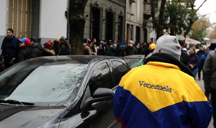 A man wears a jacket with the colours of Venezuela's national flag as other Vene