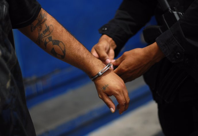 A policeman places handcuffs on a Mara Salvatrucha (MS13) gang member, who was d