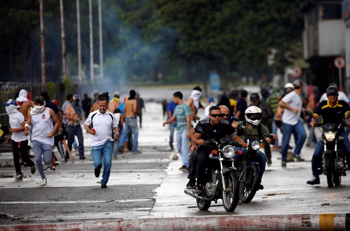 Demonstrators run and ride their motorcycles near Fuerte Paramacay military base