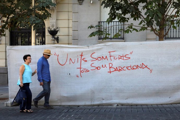 A couple walks past a graffiti that reads "United we are strong, we are all Barc