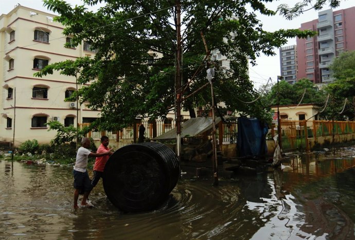 Un hombre traslada un tanque de agua en una calle parcialmente inundada en India
