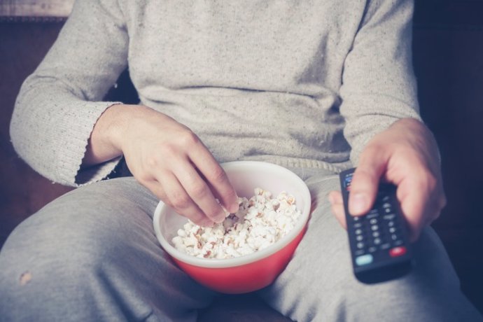 Hombre con el mando de la tele viendo una película y comiendo palomitas