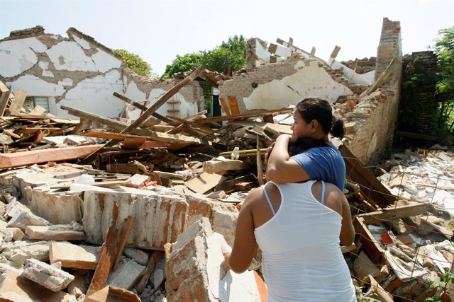 Women hug while standing next to a destroyed house after an earthquake struck th