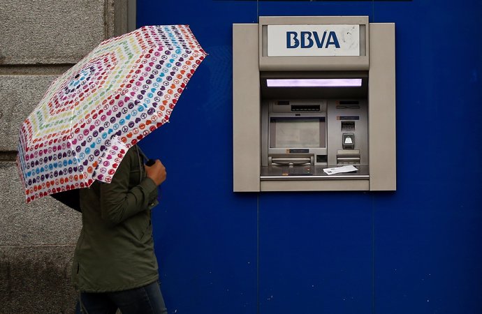 A woman with an umbrella walks past a BBVA bank branch in central Madrid, Spain,