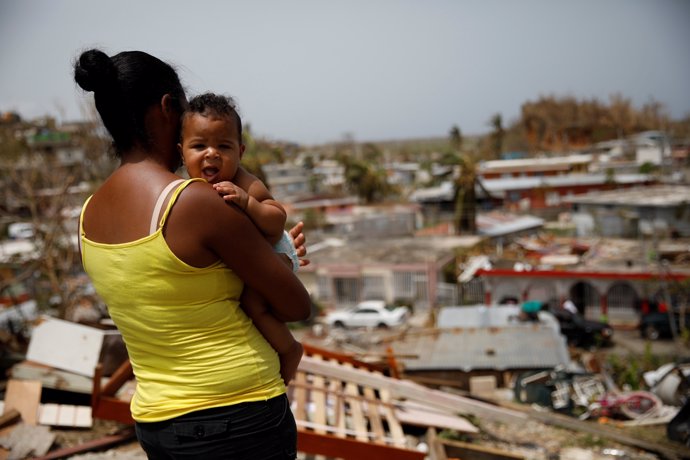 Ysamar Figueroa carrying her son Saniel, looks at the damage in the neighbourhoo