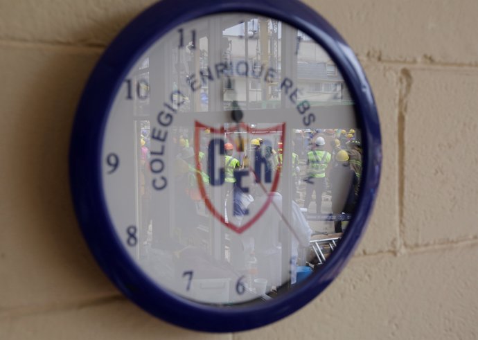 Rescue workers are reflected in the glass of a school clock during a search for 