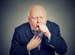 Old man coughing holding fist to mouth isolated on gray background