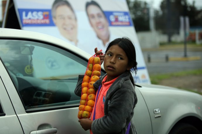 A child sells fruits near a banner of Guillermo Lasso, presidential candidate (L