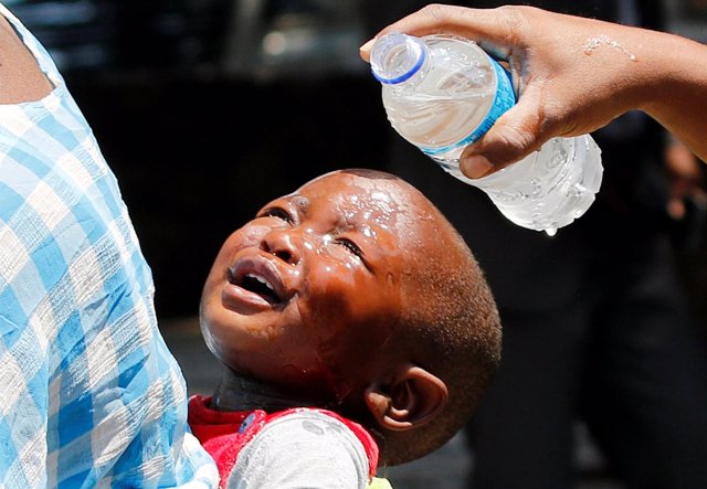 A woman pours water over a child affected by teargas after clashes between polic