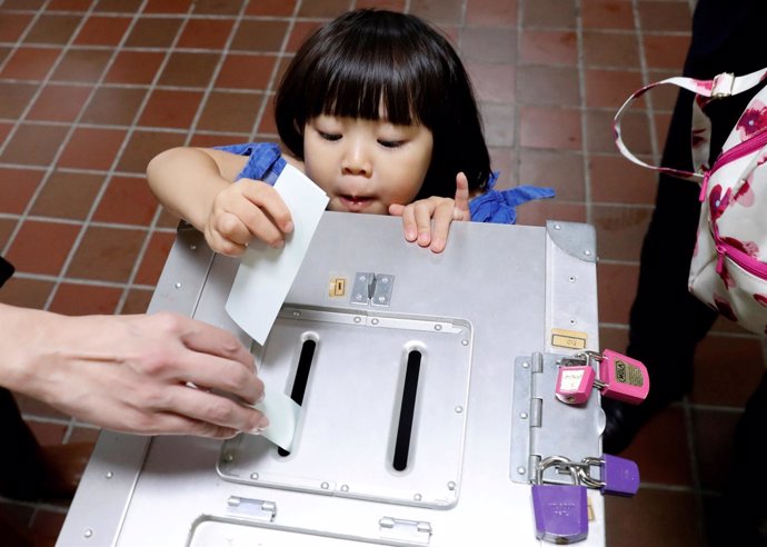 Una niña deposita el voto de su padre en las elecciones de Japón