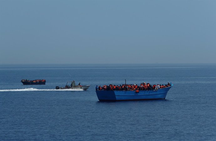 Un barco de los guardacostas libios junto a embarcaciones con inmigrantes