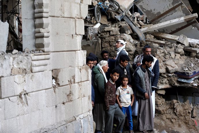 Varias personas junto a un edificio bombardeado en Saná
