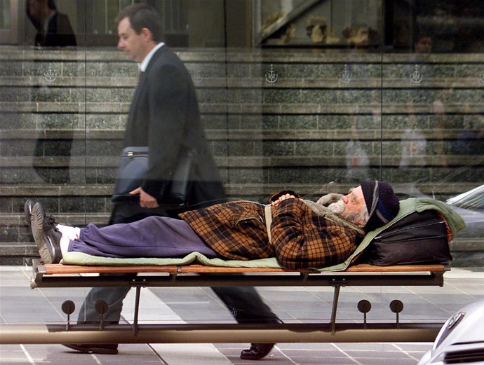 Un hombre de negocios camina mientras un indigente, pobre, descansa en un banco 
