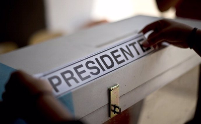 A woman places "President" stickers on ballot boxes, as a polling station is set