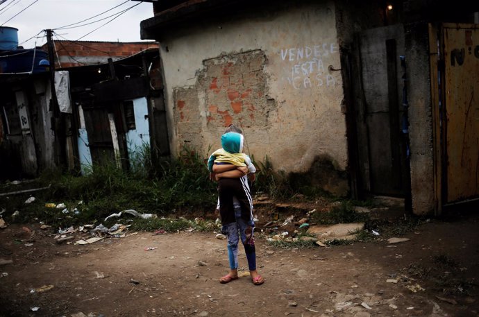 Niña brasileña con un bebé en brazos en medio de la favela en la que vive