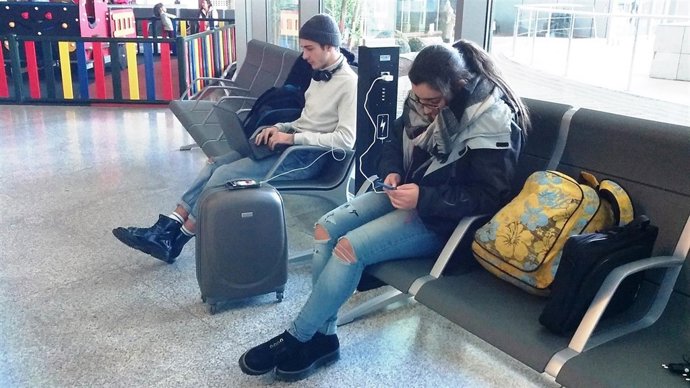 Dos turistas pasajeros aeropuerto carga móviles USB telefonos enchufes espera 