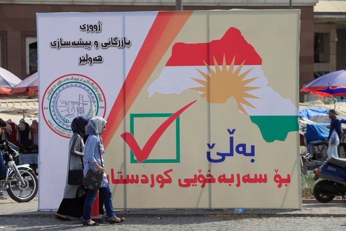 Mujeres iraquíes caminan por la calle cerca de las pancartas del referéndum del 