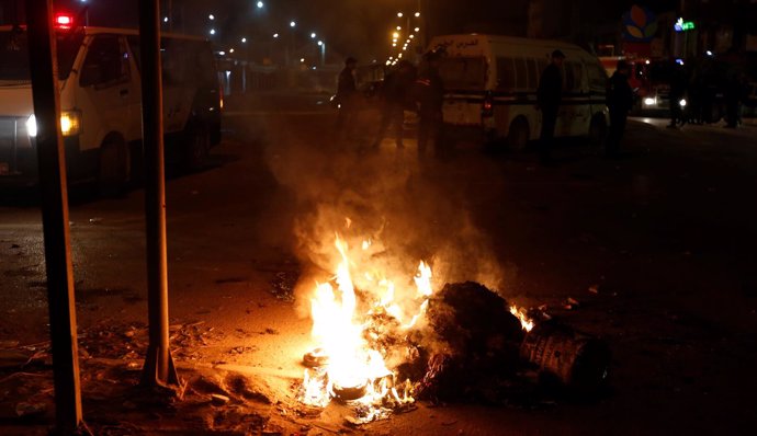 Police vehicles stop in front of burning tires set up by protesters during demon