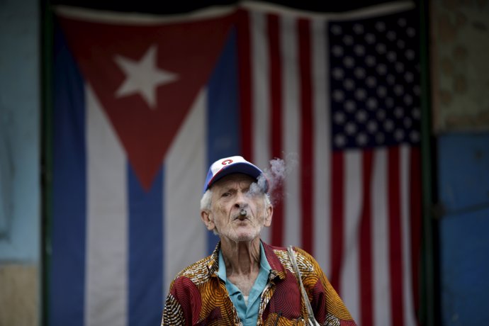 Un cubano fuma un puro ante las banderas de EEUU y Cuba