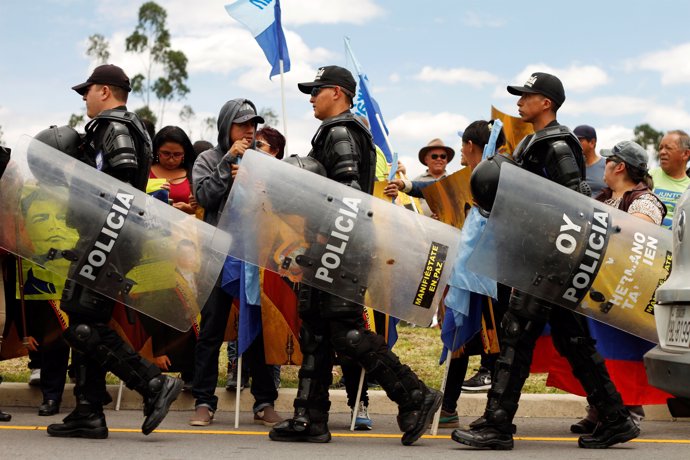 Riot police officers walk past supporters of Ecuador's former President Rafael C