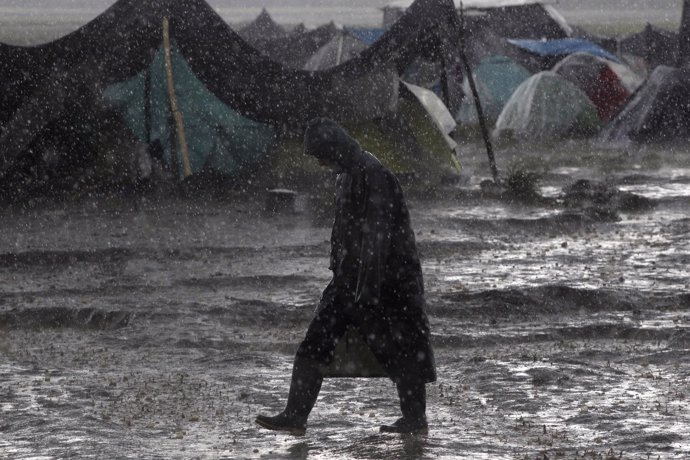 A refugee walks under heavy rainfall at a makeshift camp for migrants and refuge