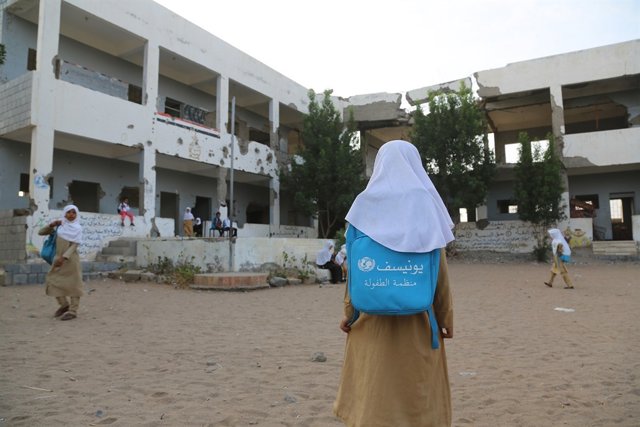 Una niña entra en el patio de una escuela dañada por el conflicto en Yemen