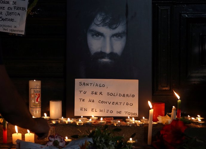 A man lights candles next to a portrait of Santiago Maldonado, a protester who w