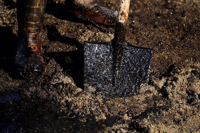 A worker's shovel is covered with oil that leaked from a small oil tanker that s