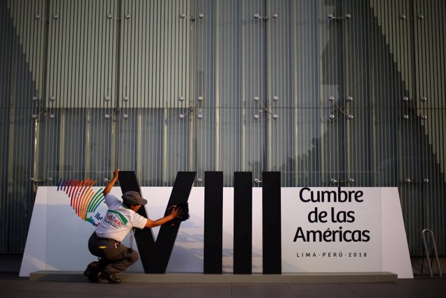 A woman cleans a banner ahead of the eighth Summit of the Americas in Lima, Peru