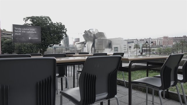 Pupitres vacíos en Bilbao con el Museo Guggenheim al fondo