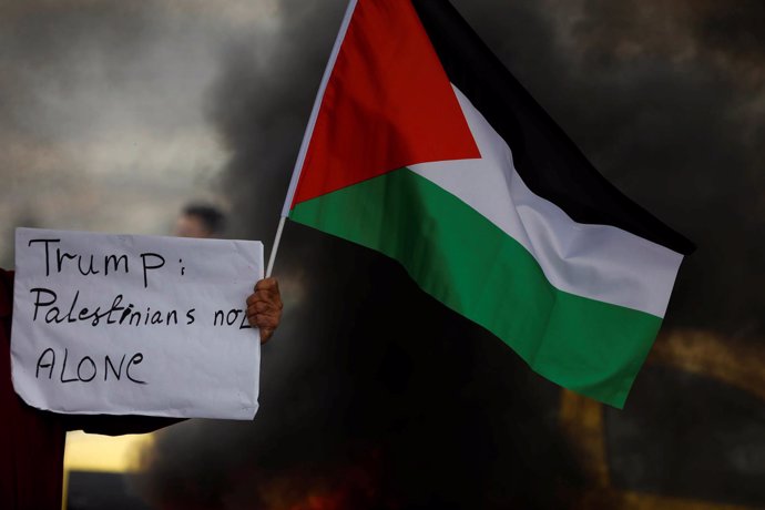 Un manifestante exhibe una bandera palestina frente a militares israelíes