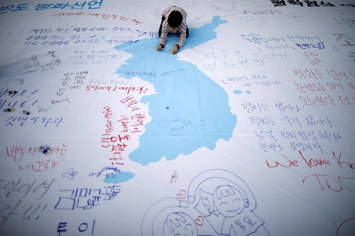 Un niño escribe un mensaje en una bandera de unificación coreana