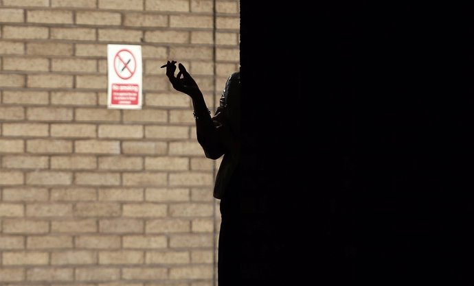 Una mujer fuma frente a una señal de "No fumar"