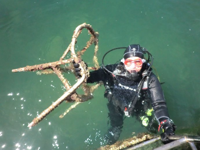 Un buceador extrae del fondo marino una vieja silla oxidada