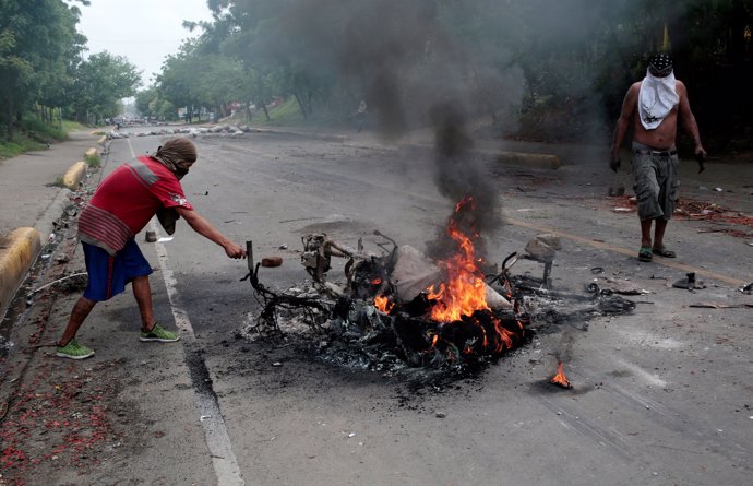 Protester stand next to a burned motorcycle during a protest against Nicaragua's